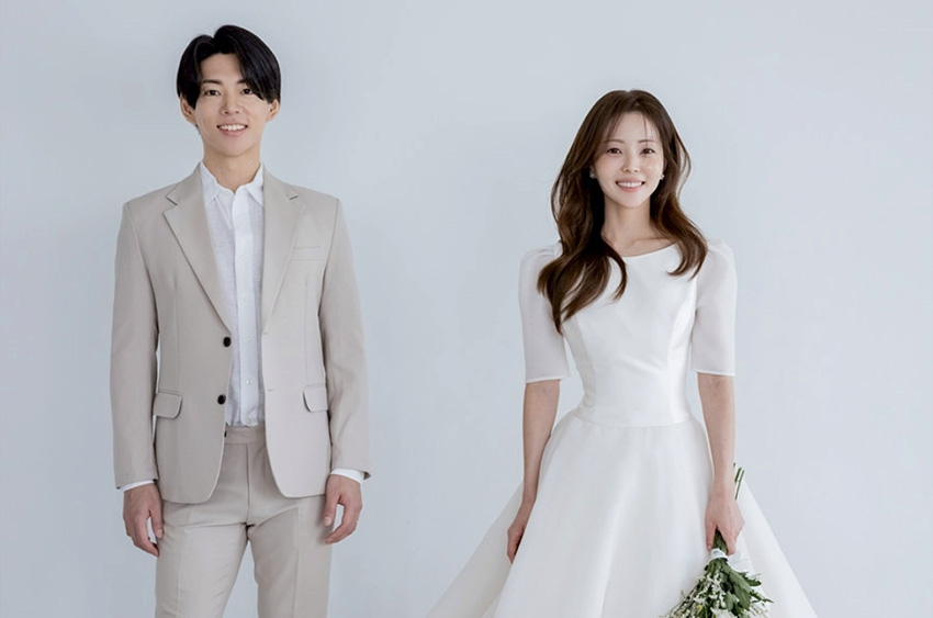 ベージュのスーツの新郎と白いドレスの新婦が並んで立つ写真