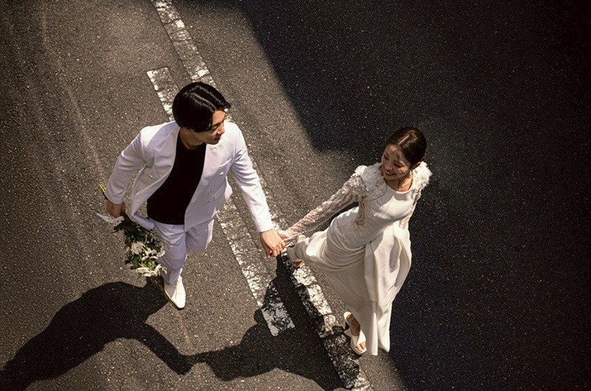 横断歩道で手をつなぐ白い衣装の新郎新婦を俯瞰で撮影した写真